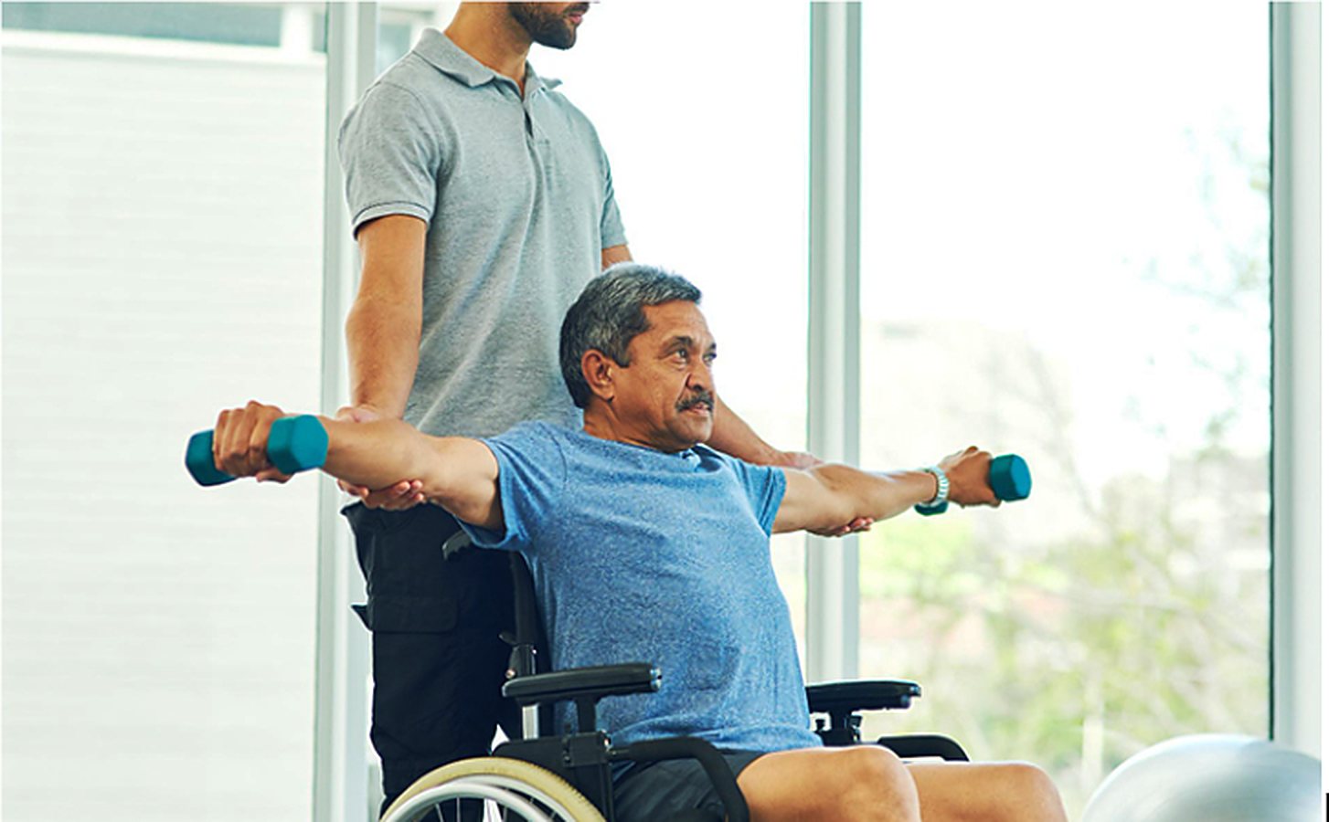 Physiotherapist guiding a man in a wheelchair through a dumbbell exercise